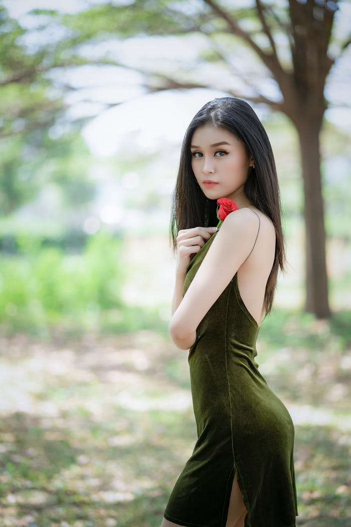 A young woman in a green dress holding a red rose in a serene outdoor setting.