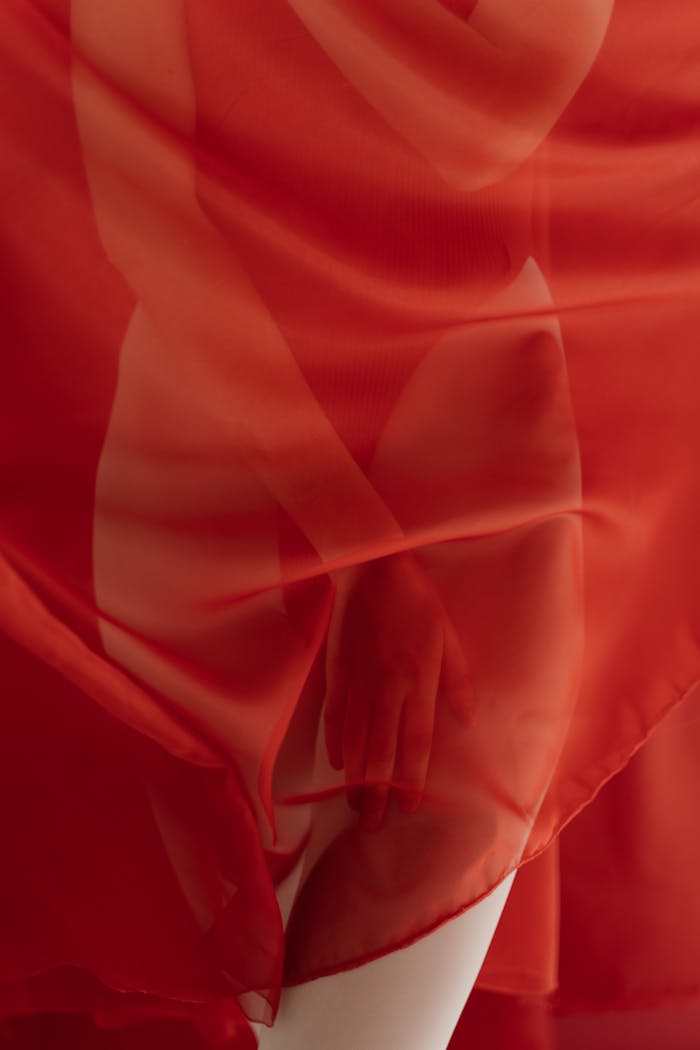 An artistic portrayal of a human figure viewed through a translucent red fabric, highlighting curves and sensuality.